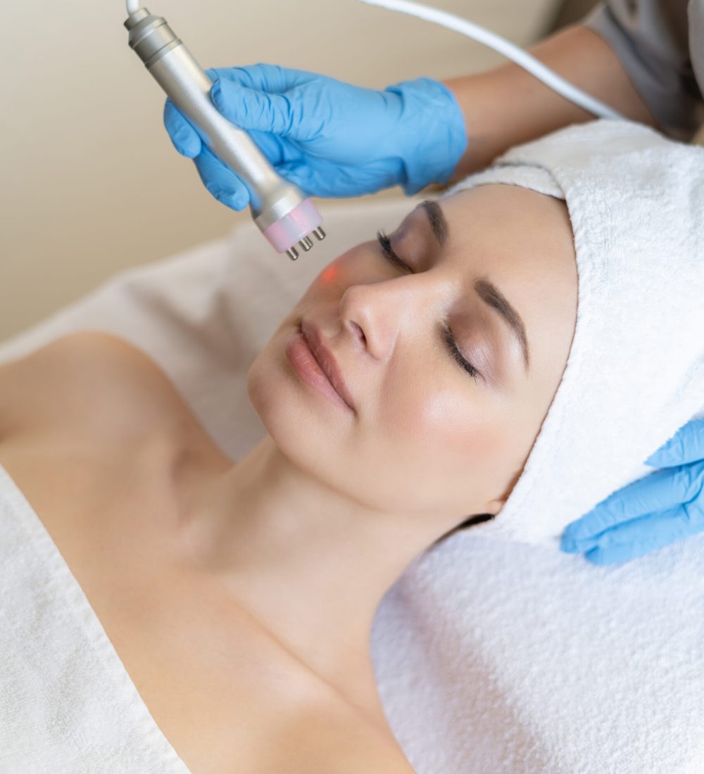 Young woman lying on cosmetologist's table during rejuvenation procedure. Cosmetologist take care about neck and face skin youthfull and wellness. Hardware face cleaning procedure